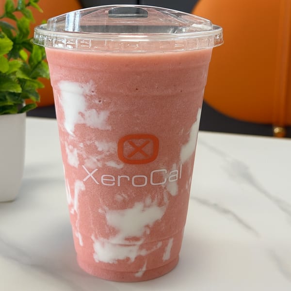 A Xerocal branded cup filled with a pink and white swirled smoothie, on a white table.