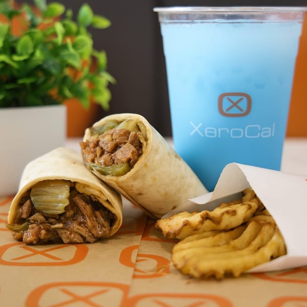 Two wraps with meat and pickles, waffle fries, and a blue drink with the Xerocal logo.
