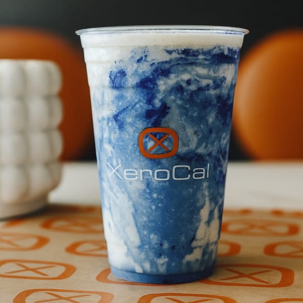 A Xerocal blue and white swirled acai-bowl drink in a clear cup on a branded table.