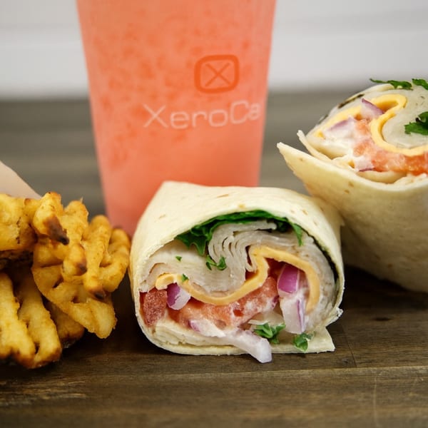 Two wraps with waffle fries and a Xerocal branded drink on a wooden surface.